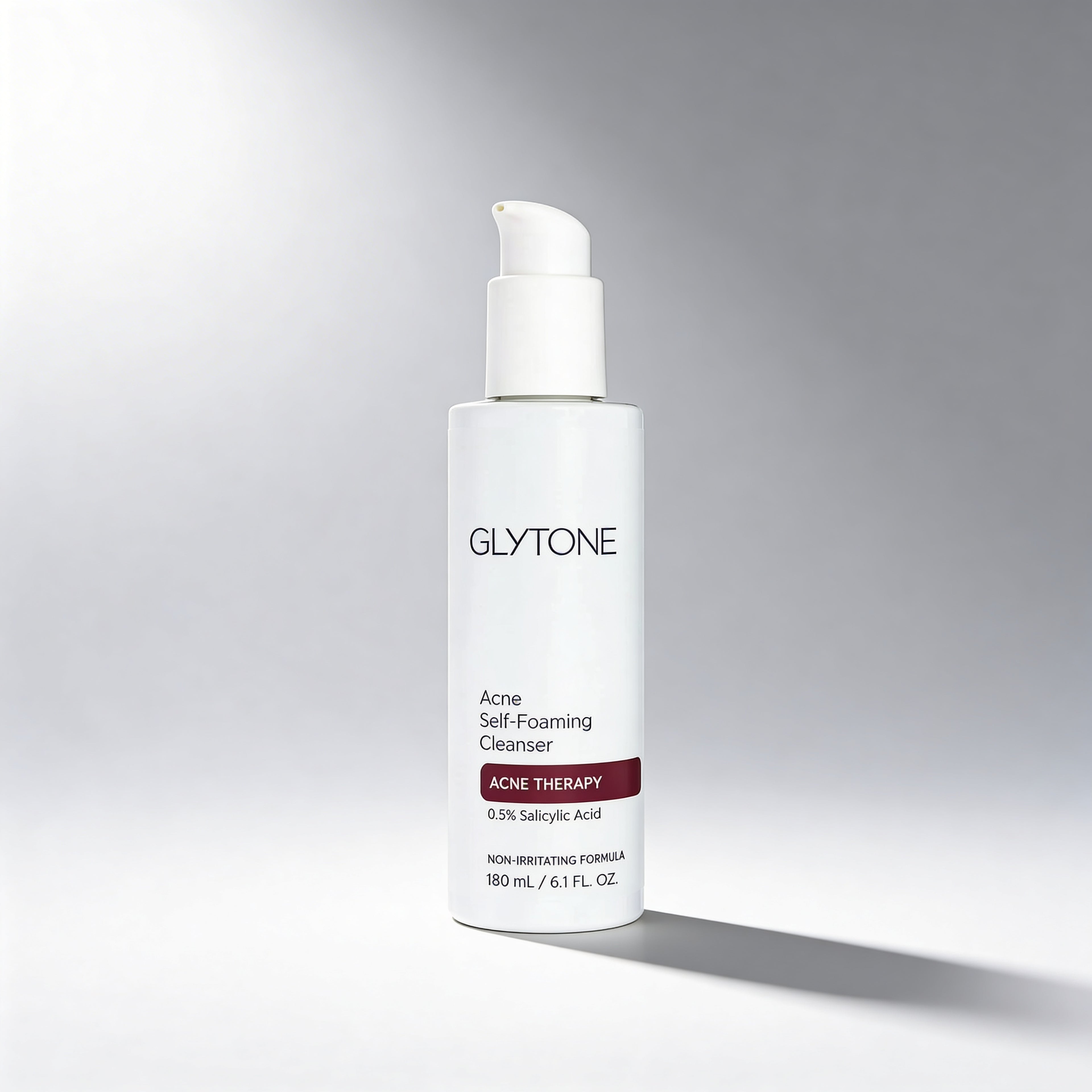 Glytone Acne Self-Foaming Cleanser bottle on a gray background