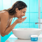 Woman washing her face with water in a bathroom, Neutrogena jar visible.