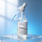 Skincare serum bottle with dropper labeled 'The Ordinary' on a clear stand against a blue gradient background.