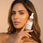 Woman holding a bottle of 'The Ordinary' serum against a beige background